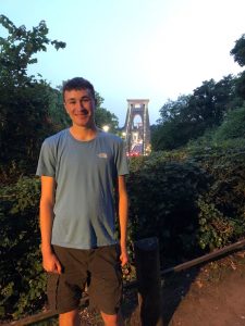 A young man in a tshirt and shorts smiling with the Clifton Suspension Bridge in the background. 