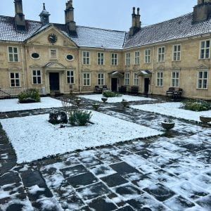 A photo of a courtyard surrounded by old stone buildings, covered in a light layer of snow.